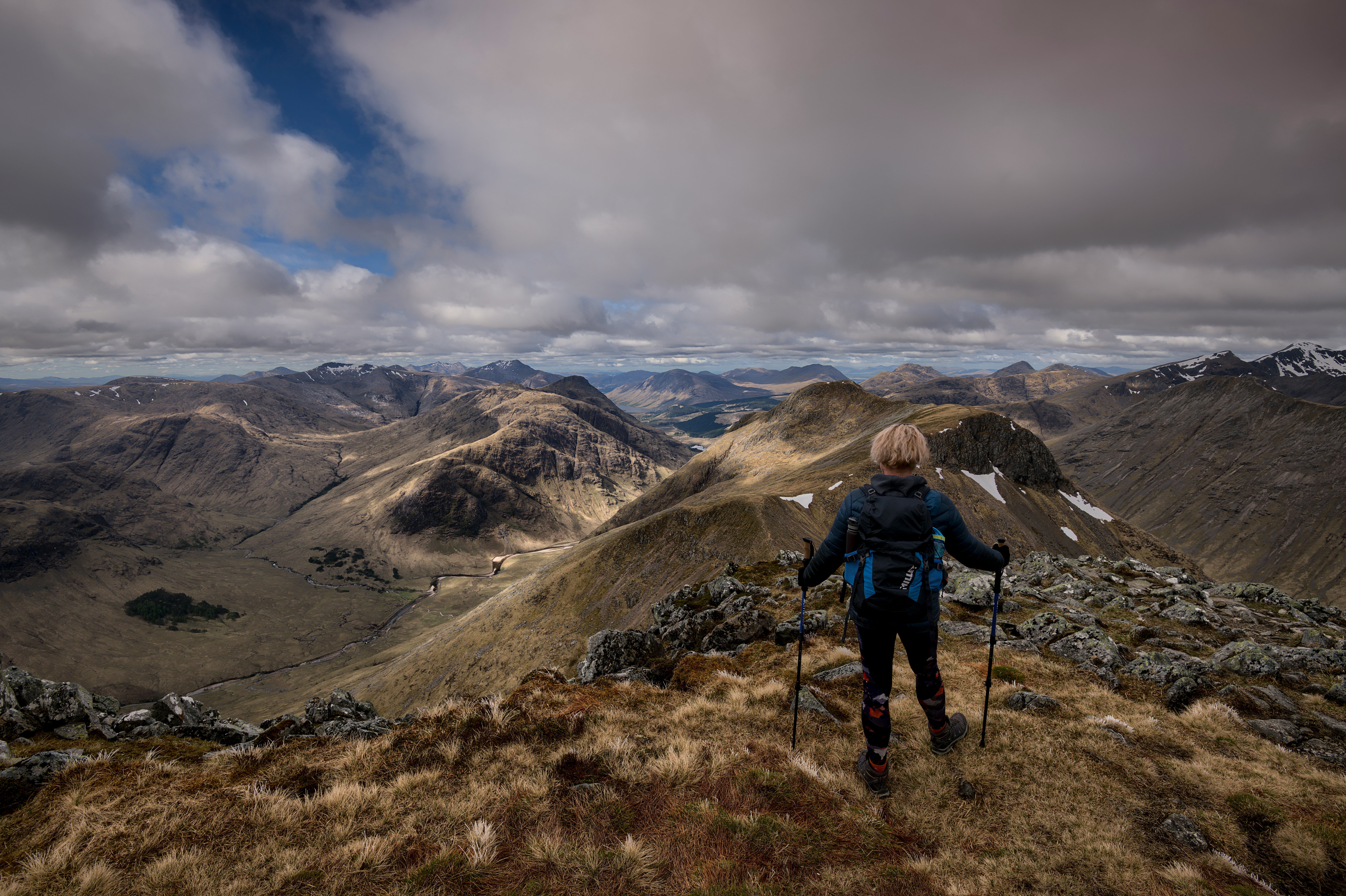 person in blue jacket and black pants with black hiking bag on mountain under white clouds